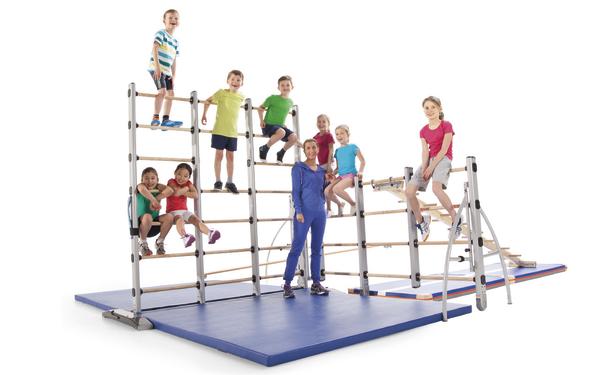 Kinder spielen und klettern an einer Turnwand mit Trainerin auf blauer Matte in Turnhalle.