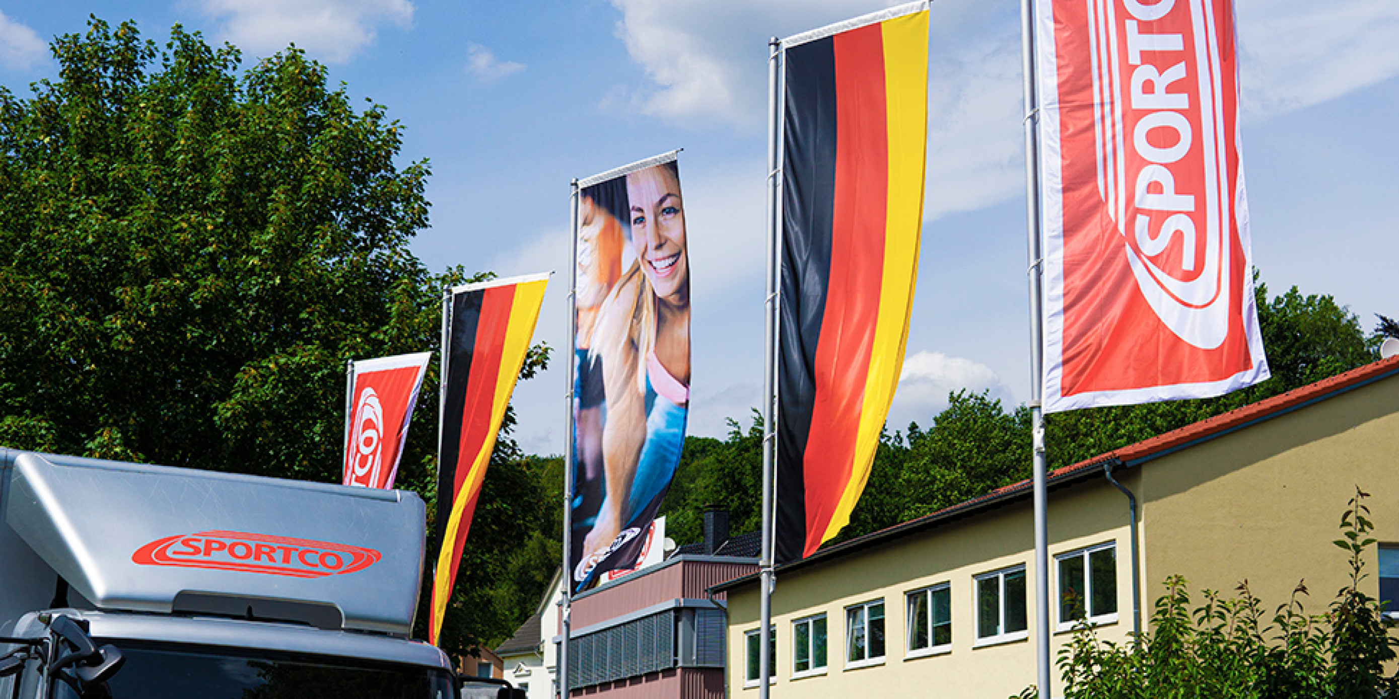 Sportco-Fahnen vor Firmengebäude mit Sportco-LKW im Vordergrund.