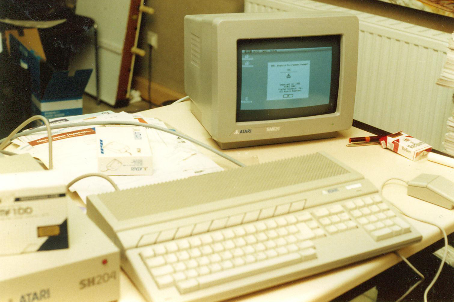 Ein alter Computer-Arbeitsplatz mit einem CRT-Monitor, einem beige Keyboard, einer Diskettenlaufwerk und einigen Schreibwaren auf dem Tisch.